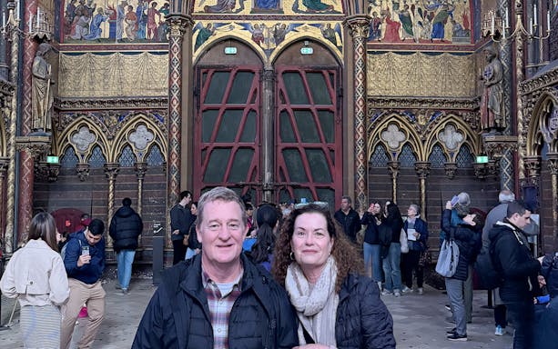 Visitors inside Sainte Chapelle, Paris, with ornate stained glass and Gothic architecture.