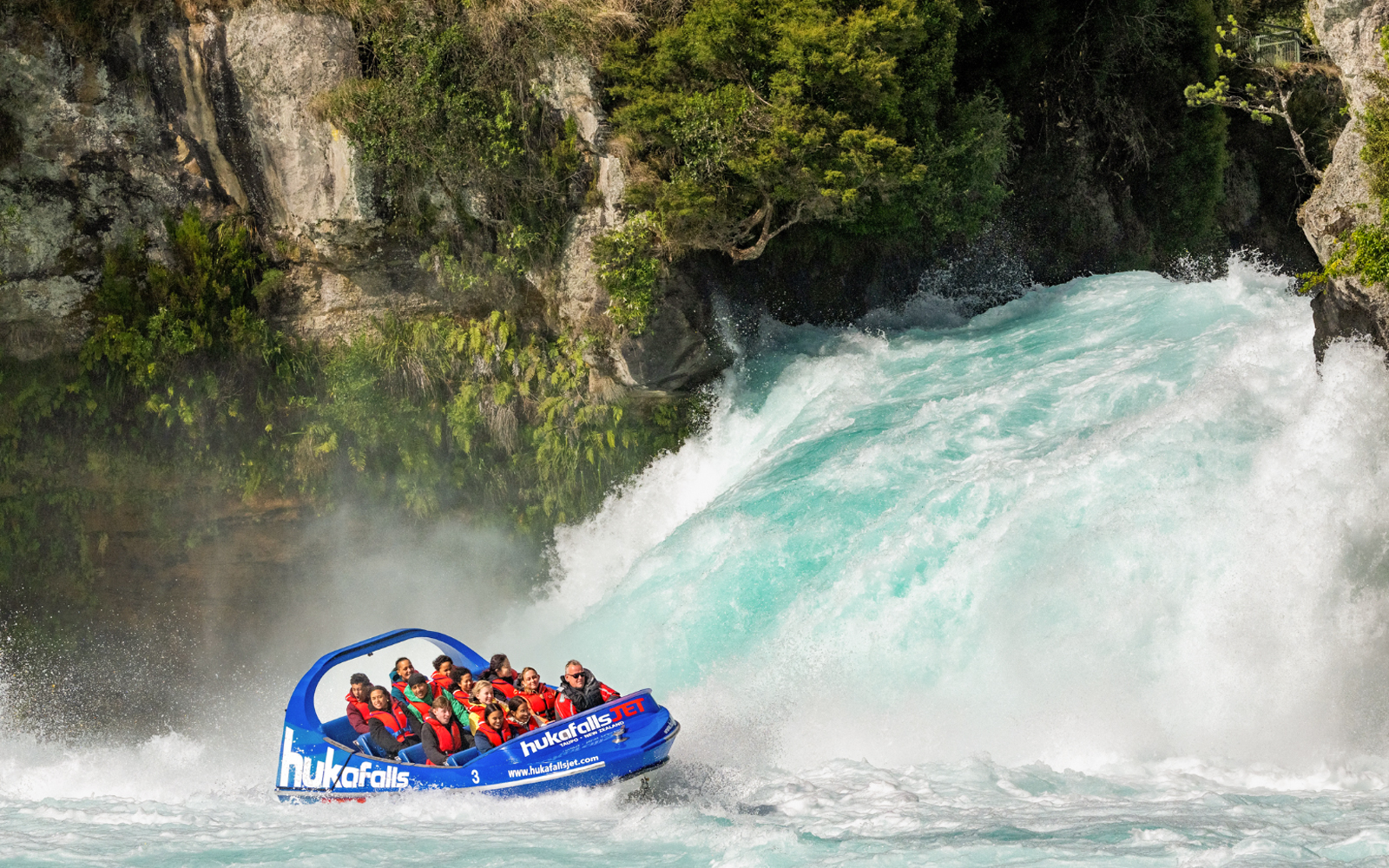 Tourists on Huka Falls jet boat ride wearing life jackets near waterfall, New Zealand.