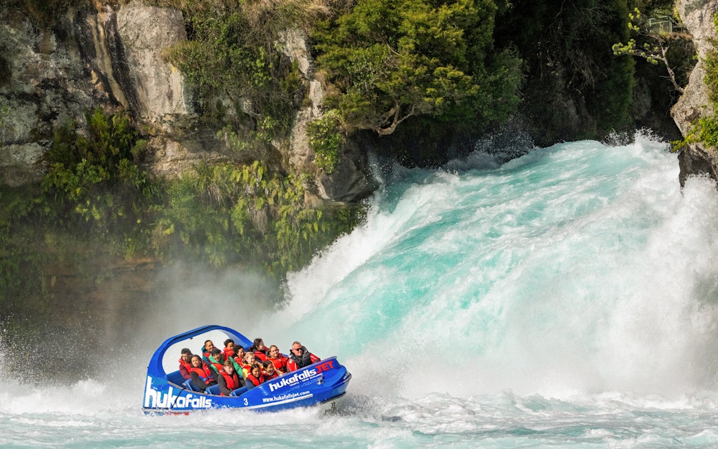 Tourists on Huka Falls jet boat ride wearing life jackets near waterfall, New Zealand.