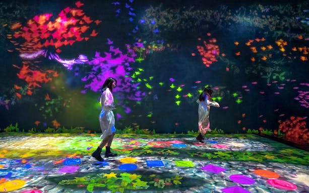 Visitors interacting with colorful digital art at teamLab Future Park.