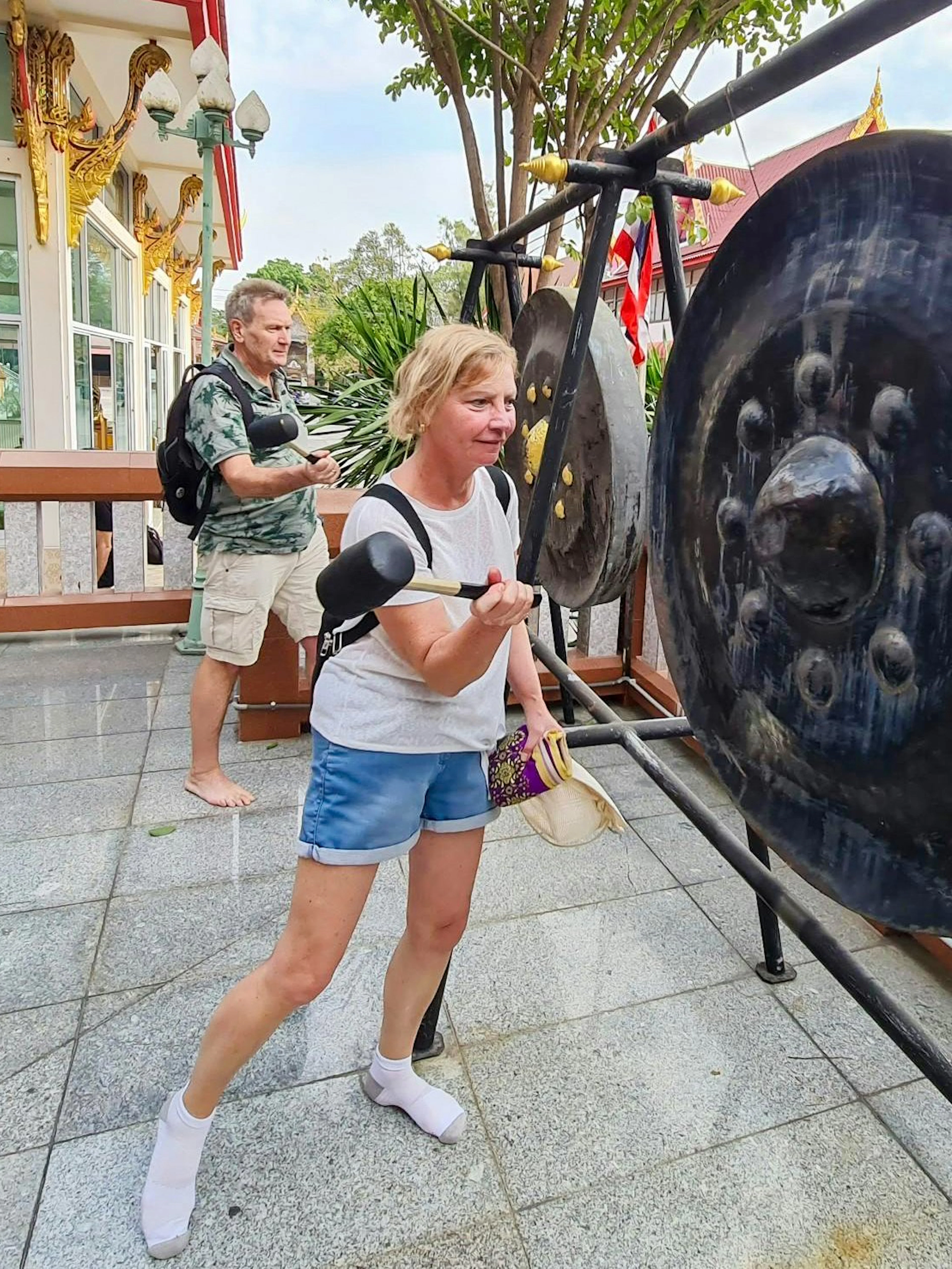 Tourists striking a large gong at a temple in Bangkok's Green Lung area.