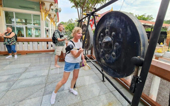 Tourists striking a large gong at a temple in Bangkok's Green Lung area.
