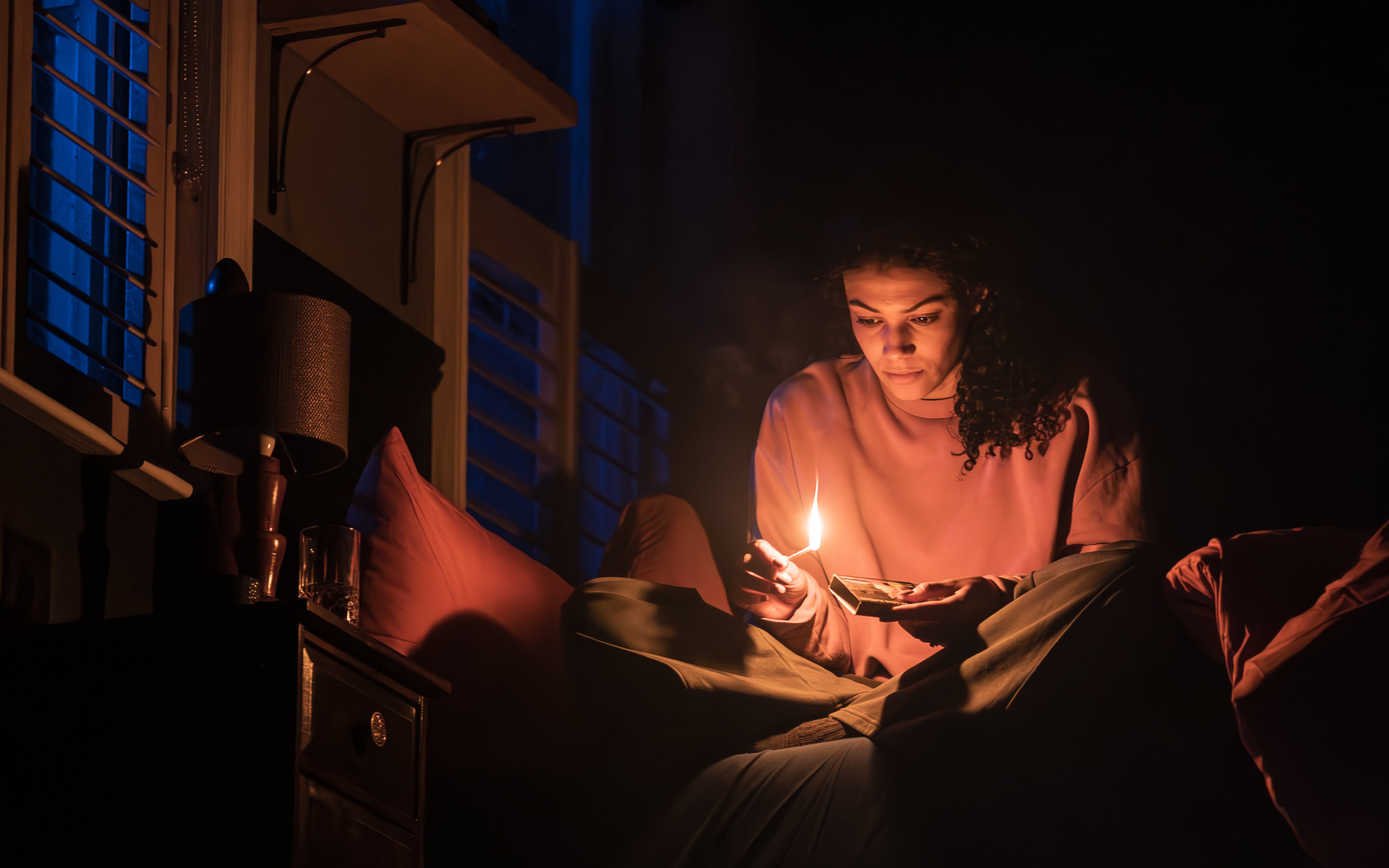 Stage scene from Paranormal Activity in Westend with person holding a lit match.