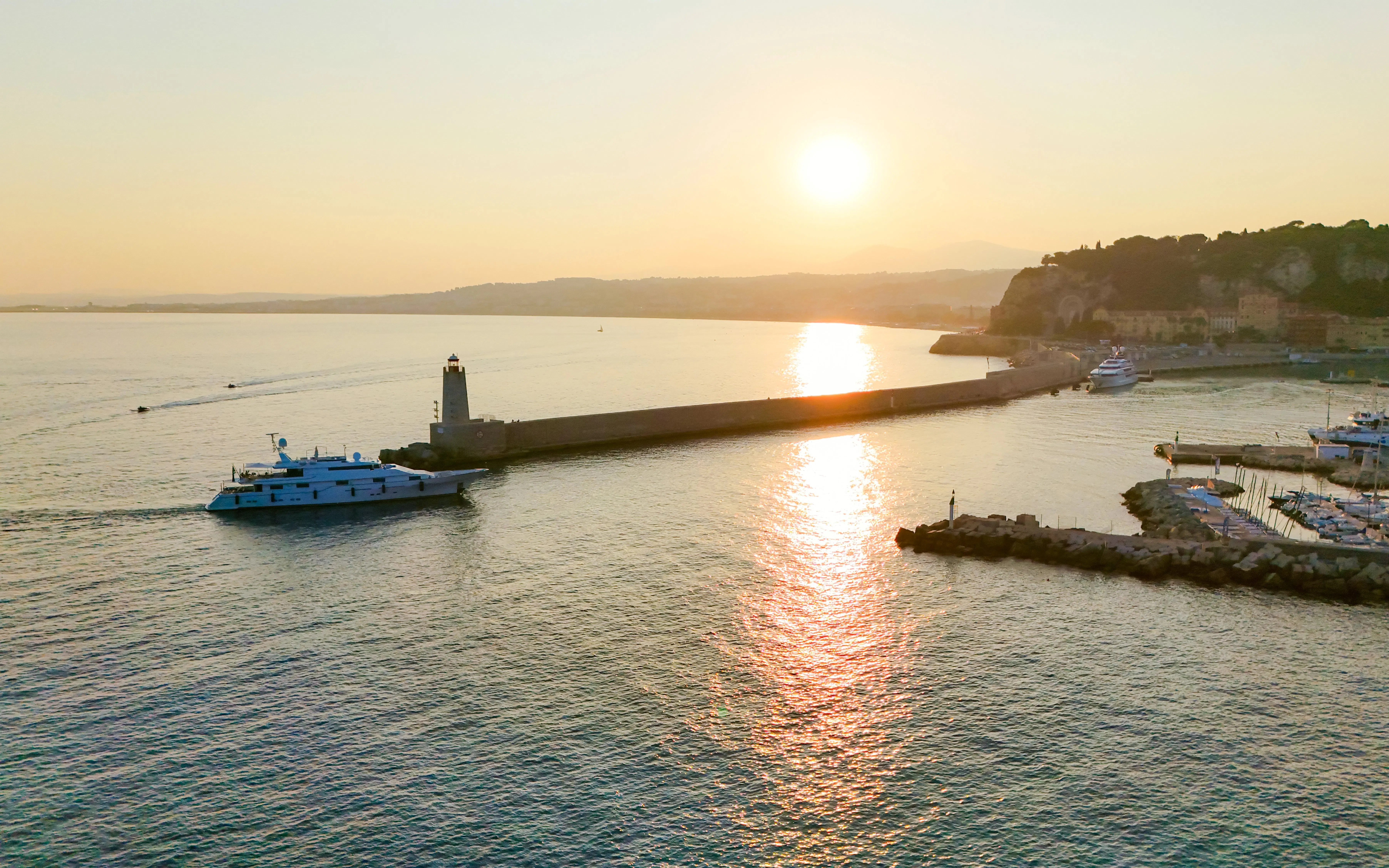 Sunrise view of a boat near the lighthouse in Nice, France, with coastal landscape.