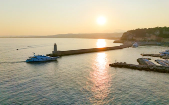 Sunrise view of a boat near the lighthouse in Nice, France, with coastal landscape.