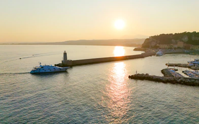 Sunrise view of a boat near the lighthouse in Nice, France, with coastal landscape.