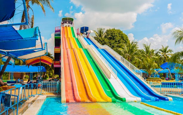 Colorful water slides at Aqualand with palm trees and blue sky.