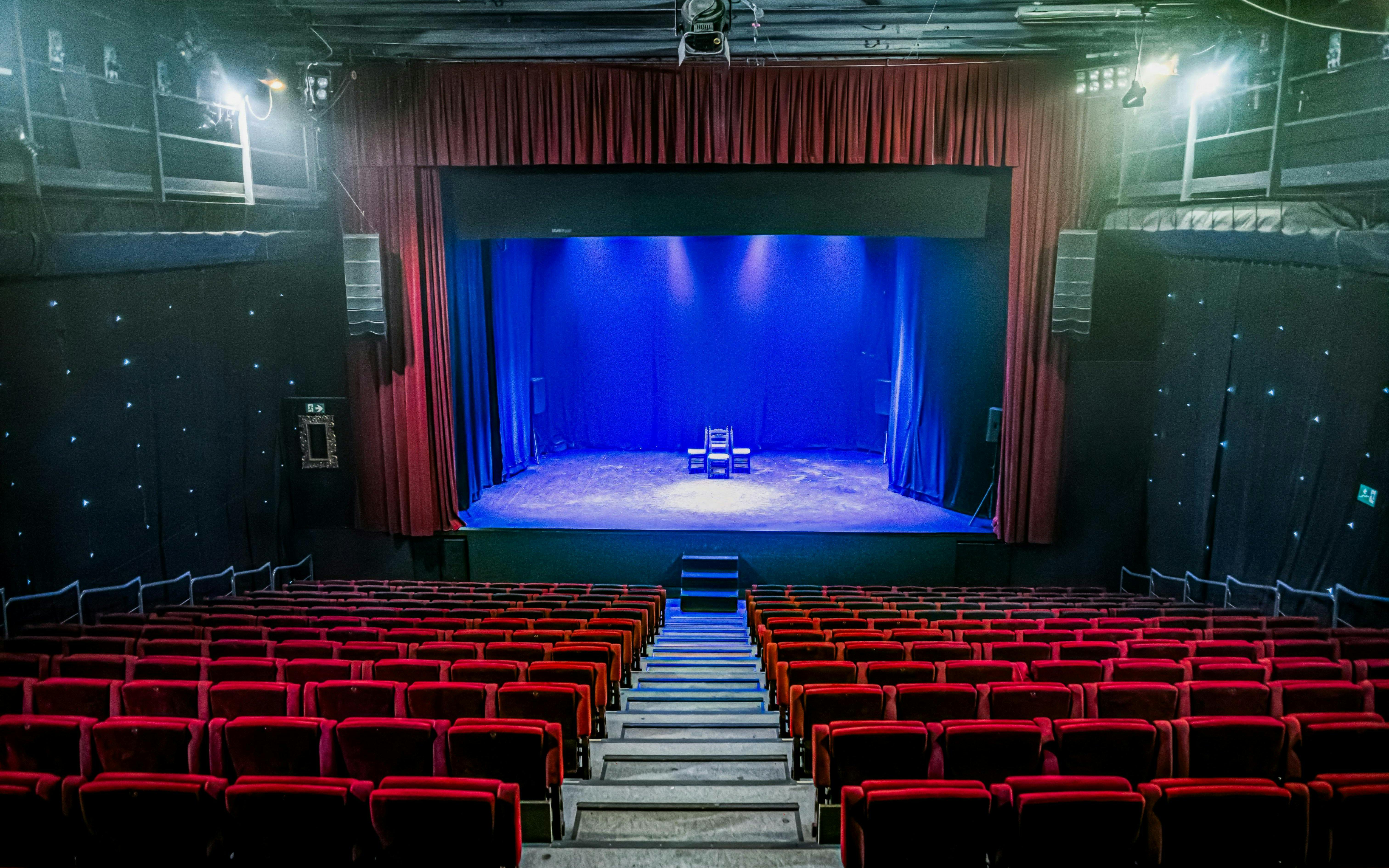 Interior of Teatro Flamenco Sevilla with empty red seats facing a lit stage.