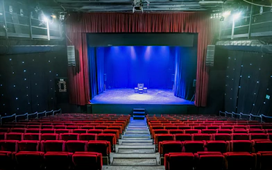 Interior of Teatro Flamenco Sevilla with empty red seats facing a lit stage.