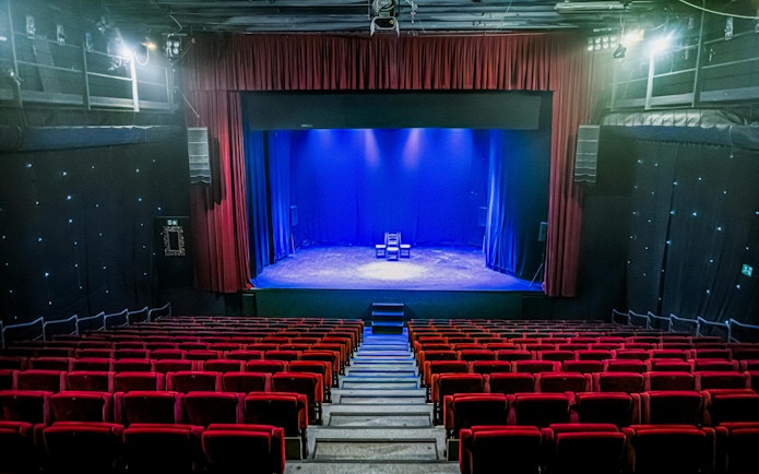 Interior of Teatro Flamenco Sevilla with empty red seats facing a lit stage.
