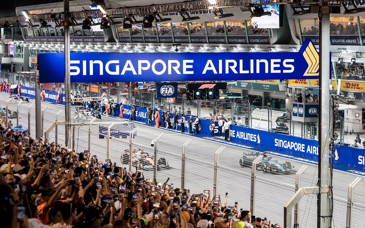 Formula 1 cars racing at Singapore Grand Prix 2025 with crowd in foreground.