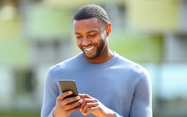Man smiling while checking his phone outdoors.