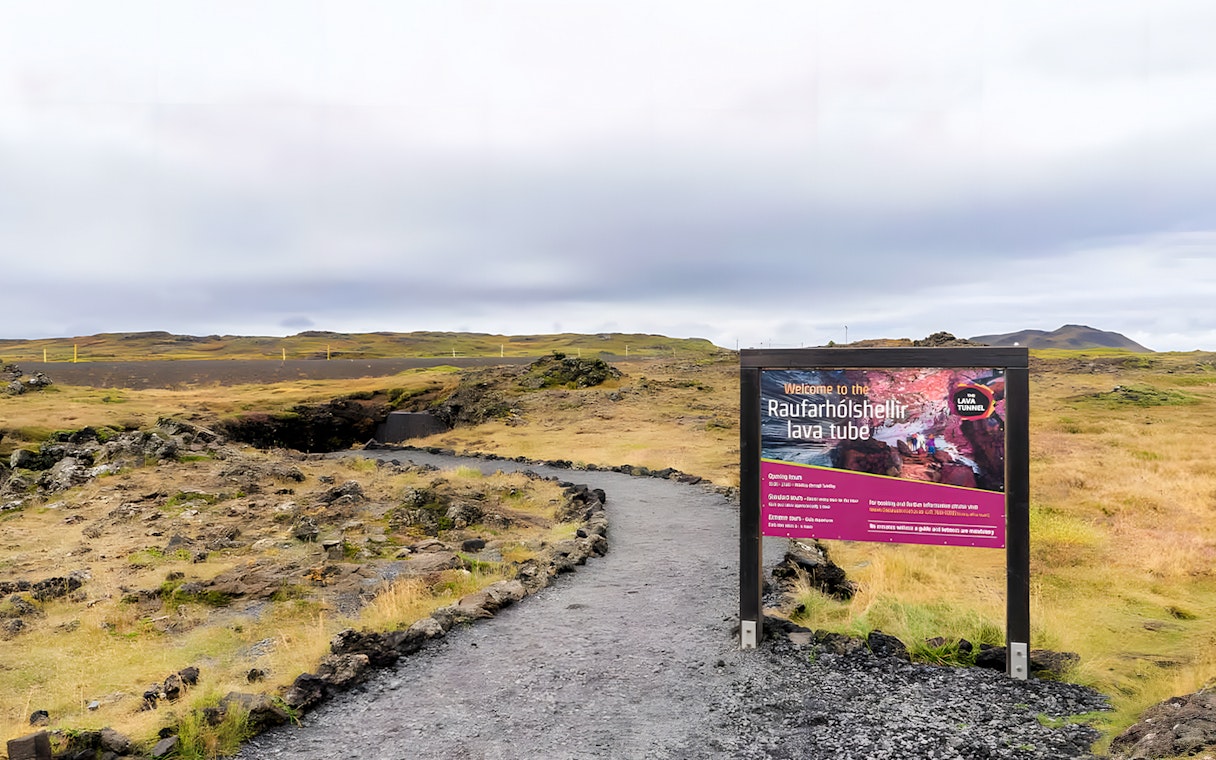 Pathway leading to the entrance of Raufarhólshellir Lava Cave, Iceland, with informational sign.