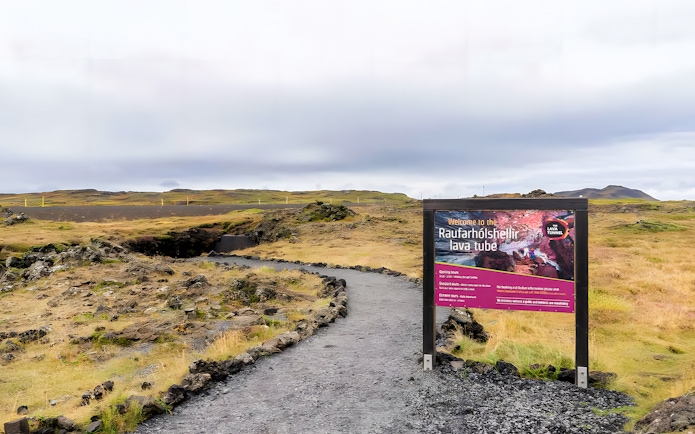 Pathway leading to the entrance of Raufarhólshellir Lava Cave, Iceland, with informational sign.