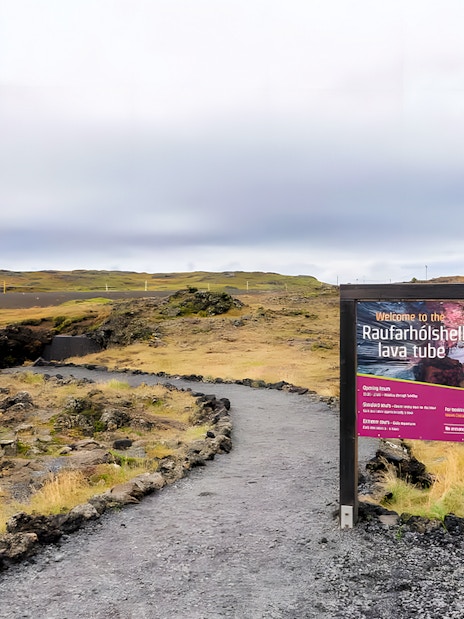 Pathway leading to the entrance of Raufarhólshellir Lava Cave, Iceland, with informational sign.