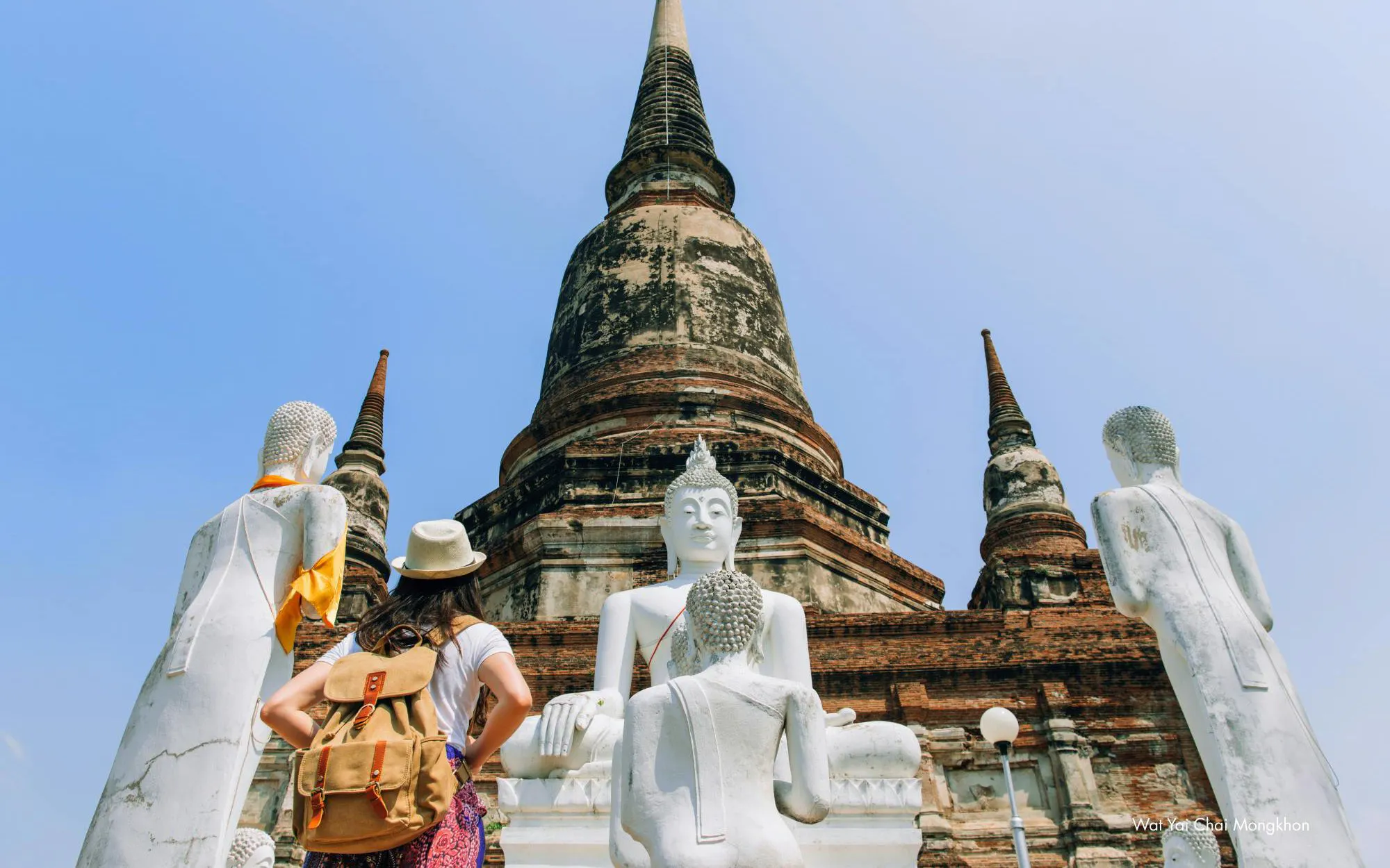 Traveler exploring Wat Yai Chai Mongkol with Buddha statues and ancient stupa in Ayutthaya, Thailand.