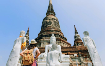 Traveler exploring Wat Yai Chai Mongkol with Buddha statues and ancient stupa in Ayutthaya, Thailand.