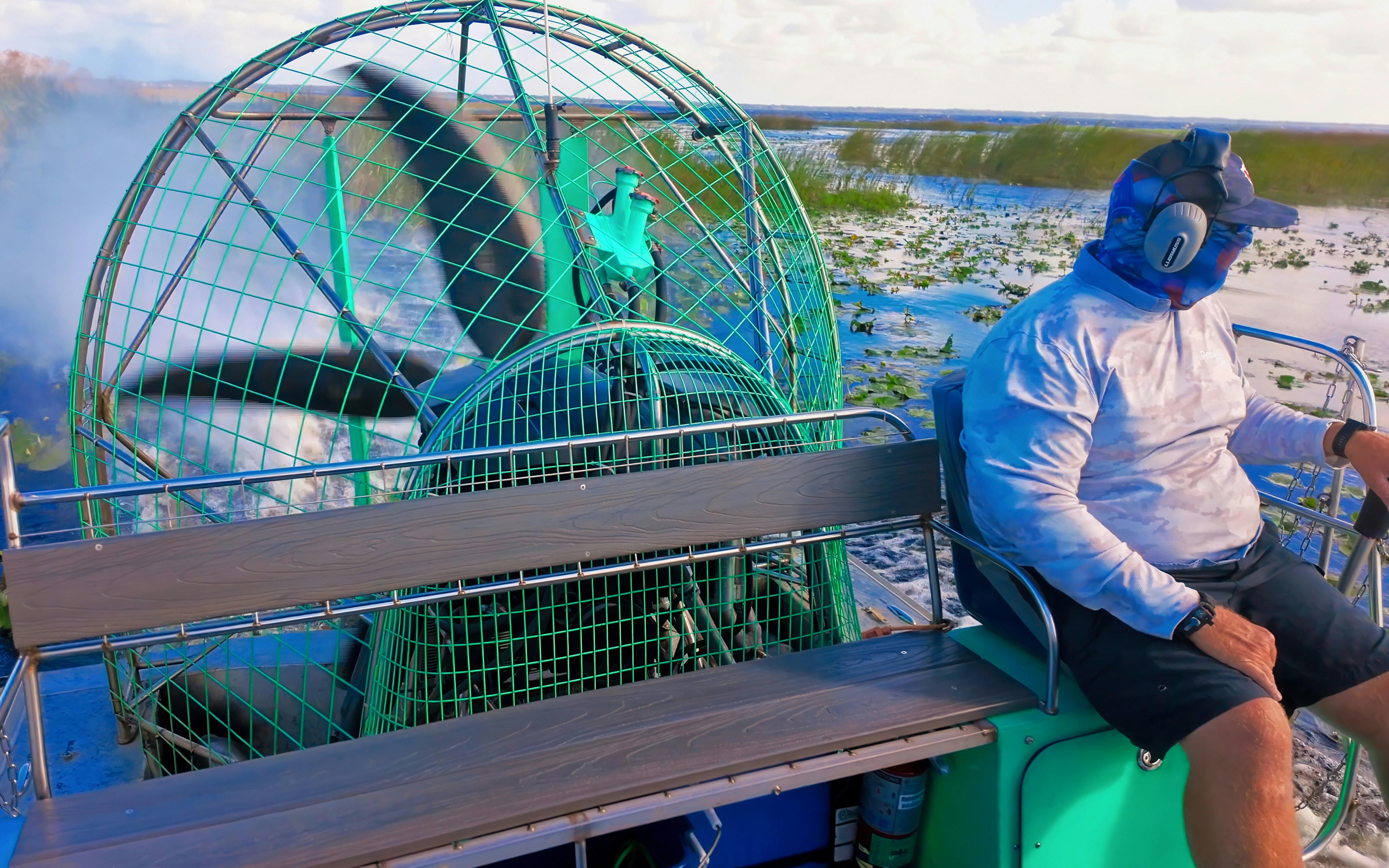 Airboat navigating through Everglades with passenger wearing headphones.