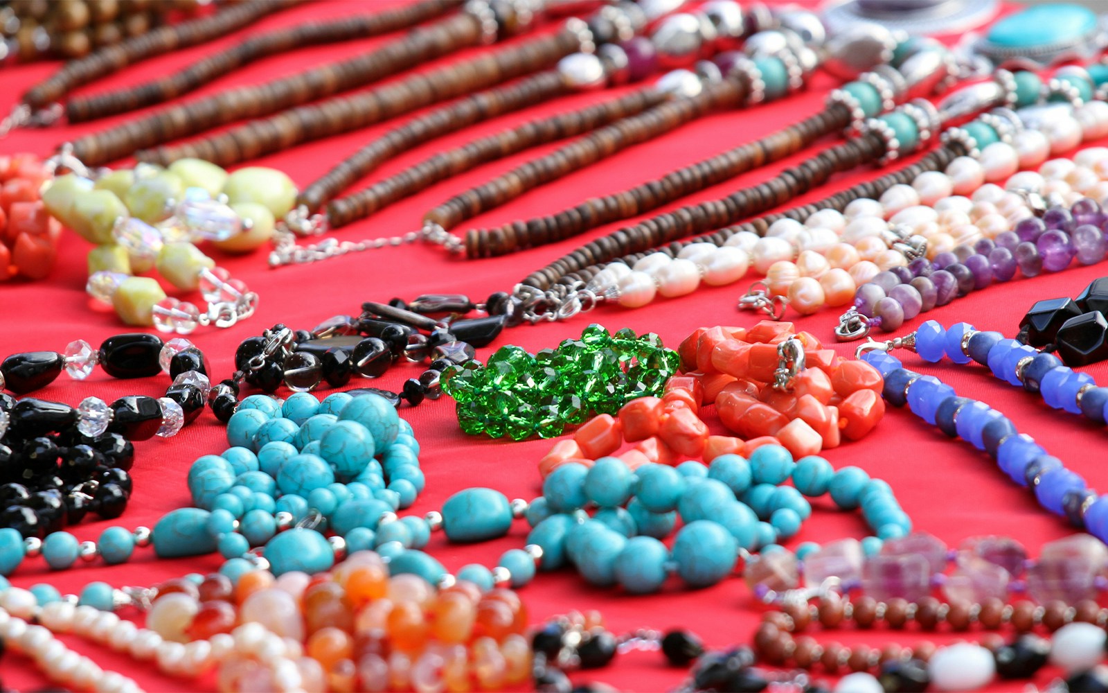 Colorful gemstone necklaces displayed on a red cloth in a Rome market.