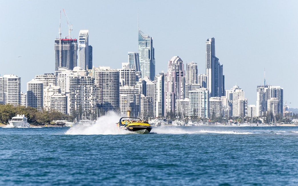 Jet boat speeding on water with city skyline in the background, part of Jet Boat Adventure Ride & Aquaduck Safari Combo.