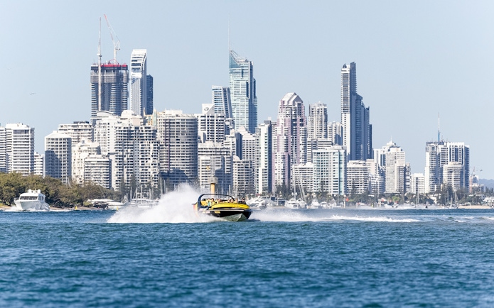 Jet boat speeding on water with city skyline in the background, part of Jet Boat Adventure Ride & Aquaduck Safari Combo.
