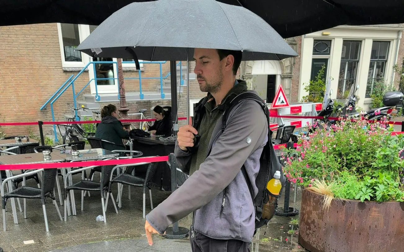 Man with umbrella walking past outdoor café in Amsterdam.