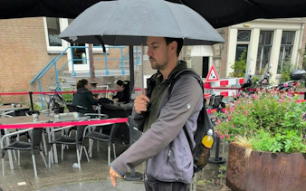 Man with umbrella walking past outdoor café in Amsterdam.