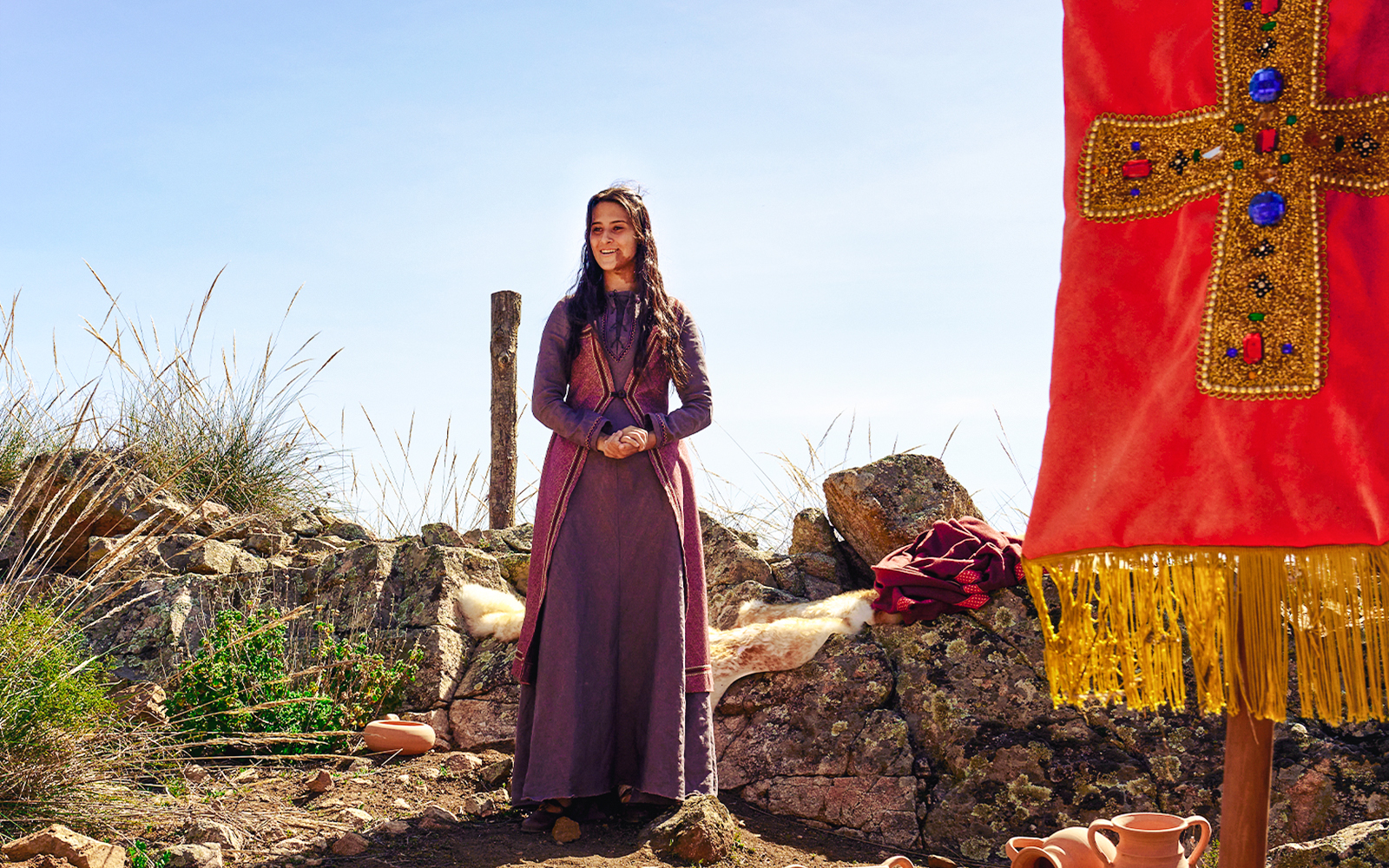 Woman in historical attire at De Tal Palo, Puy du Fou, standing by rocks and pottery.