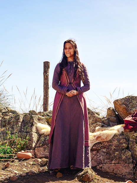 Woman in historical attire at De Tal Palo, Puy du Fou, standing by rocks and pottery.