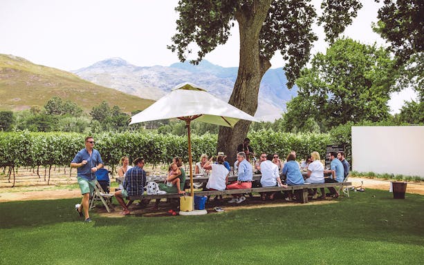 Group enjoying wine tasting under umbrella on Franschhoek Wine Tram Xplorer Tour, Cape Town.