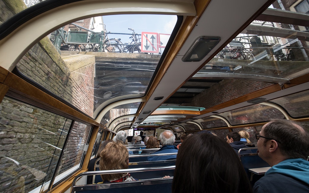 Passengers on Amsterdam canal cruise boat passing under a bridge near A'DAM Tower.