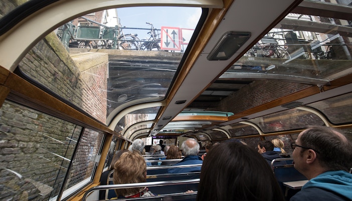 Passengers on Amsterdam canal cruise boat passing under a bridge near A'DAM Tower.