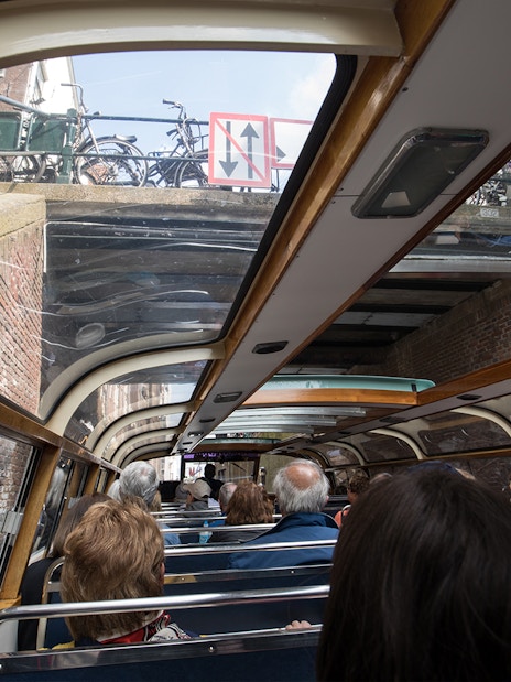 Passengers on Amsterdam canal cruise boat passing under a bridge near A'DAM Tower.