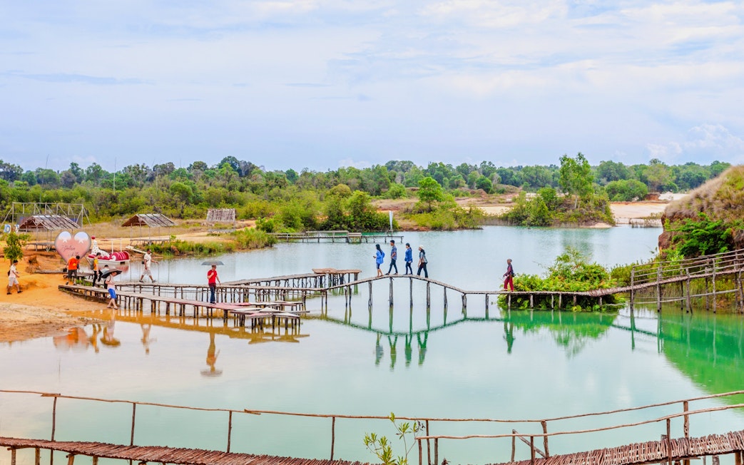People walking on a wooden bridge over Blue Lake in Bintan, surrounded by greenery.