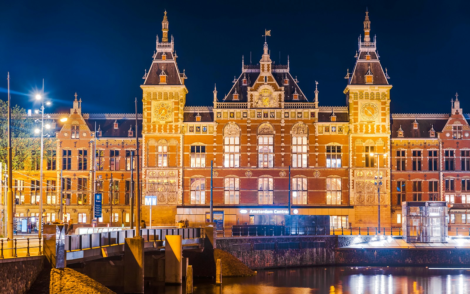 Amsterdam Central Station illuminated at night, reflecting in the canal, Netherlands.