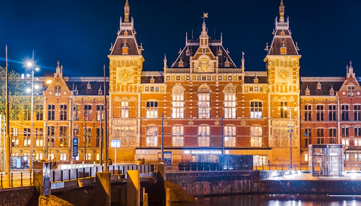 Amsterdam Central Station illuminated at night, reflecting in the canal, Netherlands.