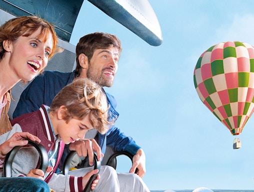 Family enjoying a ride at Futuroscope with a hot air balloon in the background.