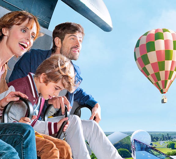Family enjoying a ride at Futuroscope with a hot air balloon in the background.