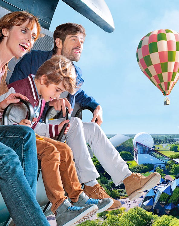 Family enjoying a ride at Futuroscope with a hot air balloon in the background.