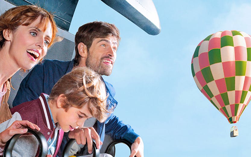 Family enjoying a ride at Futuroscope with a hot air balloon in the background.