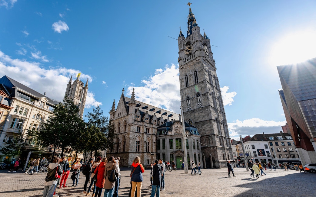 Belfry of Ghent in historic city center, Belgium, with tourists exploring the square.