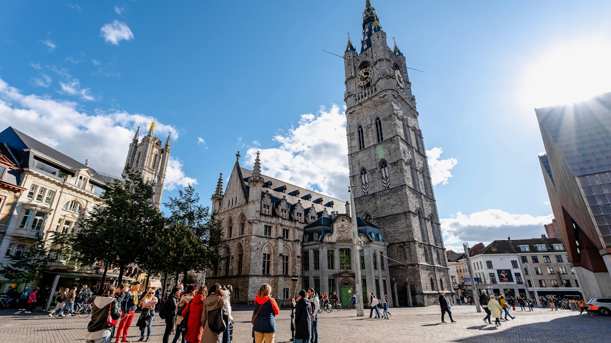 Belfry of Ghent in historic city center, Belgium, with tourists exploring the square.