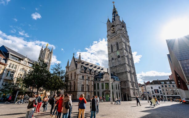 Belfry of Ghent in historic city center, Belgium, with tourists exploring the square.