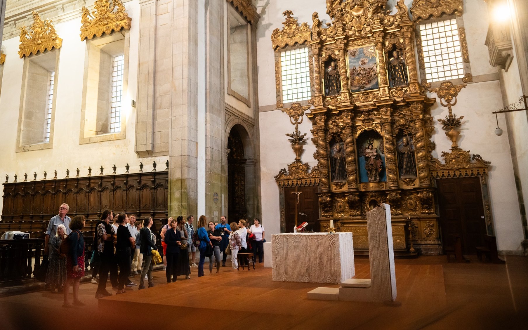 Tourists with guide inside Monastery of São Bento da Vitória, ornate altar in background.