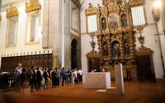 Tourists with guide inside Monastery of São Bento da Vitória, ornate altar in background.