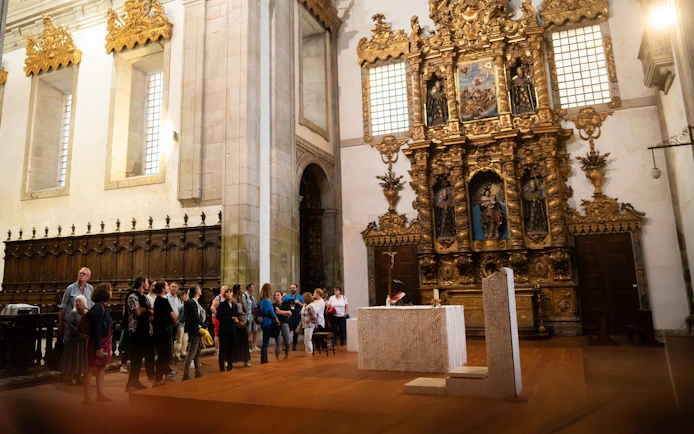 Tourists with guide inside Monastery of São Bento da Vitória, ornate altar in background.