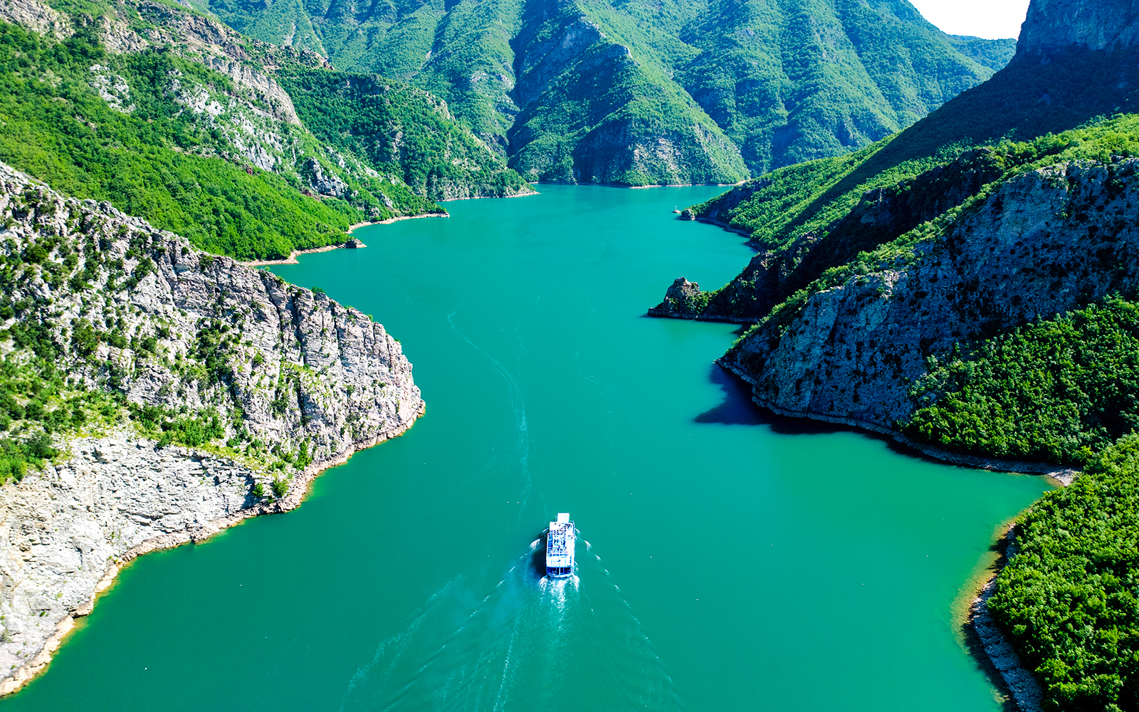 Boat cruising through Komani Lake surrounded by lush mountains in Albania.