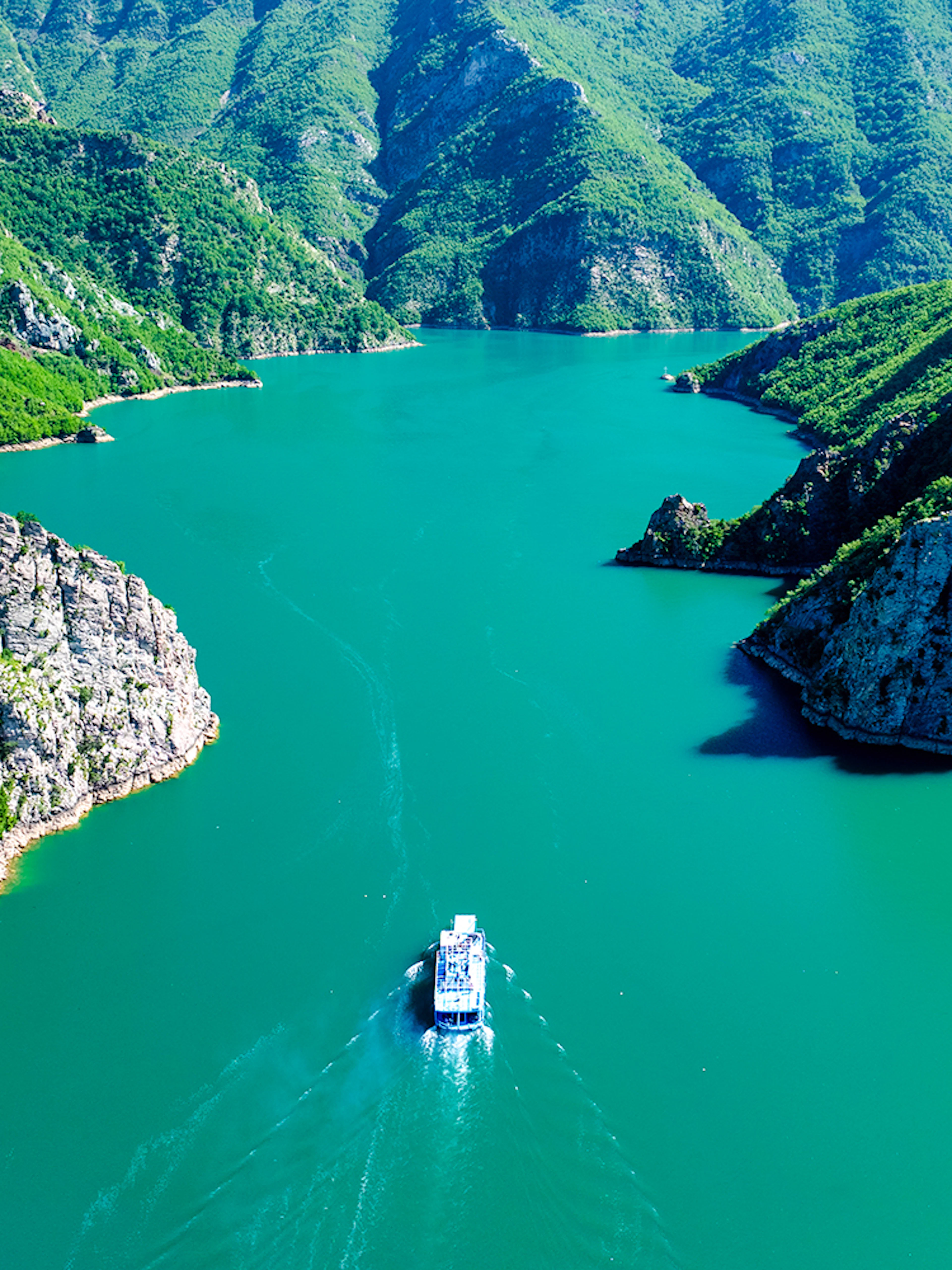 Boat cruising through Komani Lake surrounded by lush mountains in Albania.