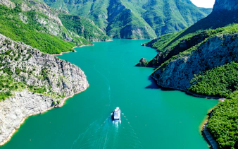 Boat cruising through Komani Lake surrounded by lush mountains in Albania.