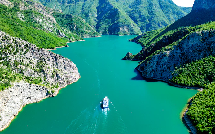 Boat cruising through Komani Lake surrounded by lush mountains in Albania.